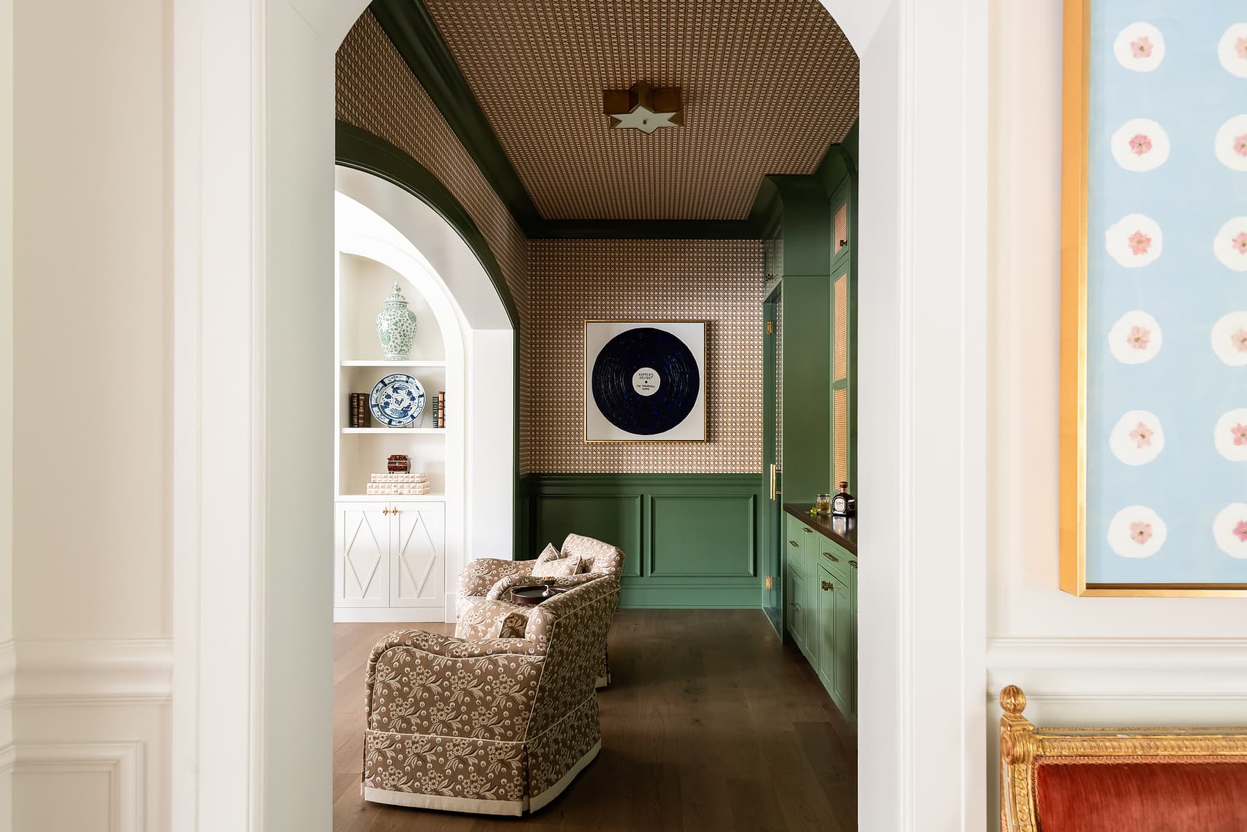 Elegant transitional hallway with arched doorway, green millwork, patterned wallpaper, and upholstered bench in a refined residential interior