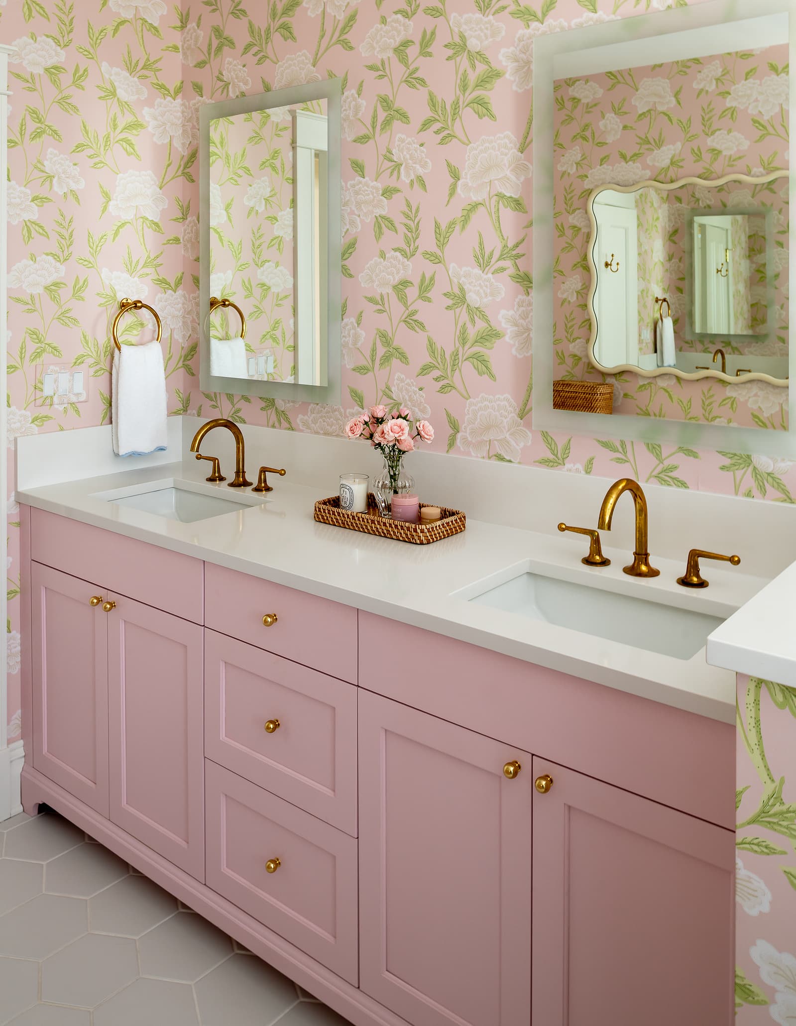 Soft pink bathroom vanity with brass fixtures, floral wallpaper, and dual mirrors in a light, feminine residential design