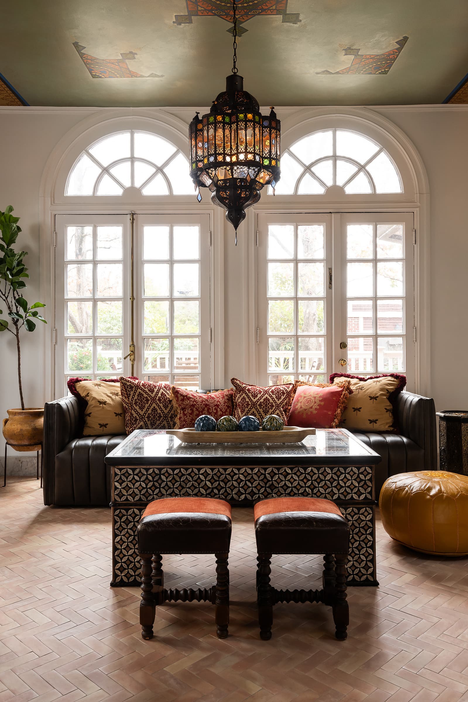 Traditional living room with arched windows, patterned ceiling, chandelier, and layered seating in a warm, collected interior