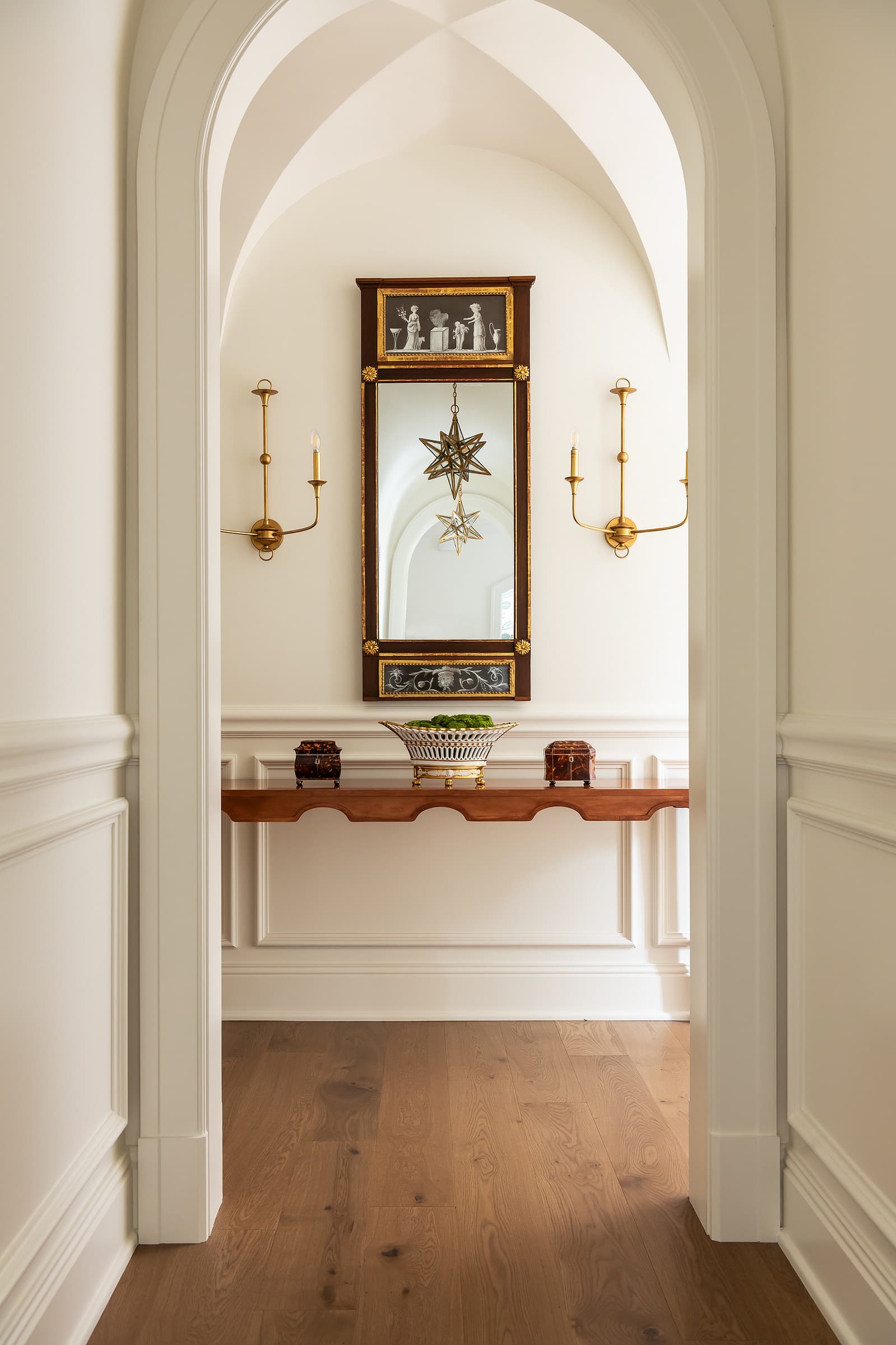 Arched hallway with console table, wall sconces, and framed artwork creating a symmetrical transitional interior vignette